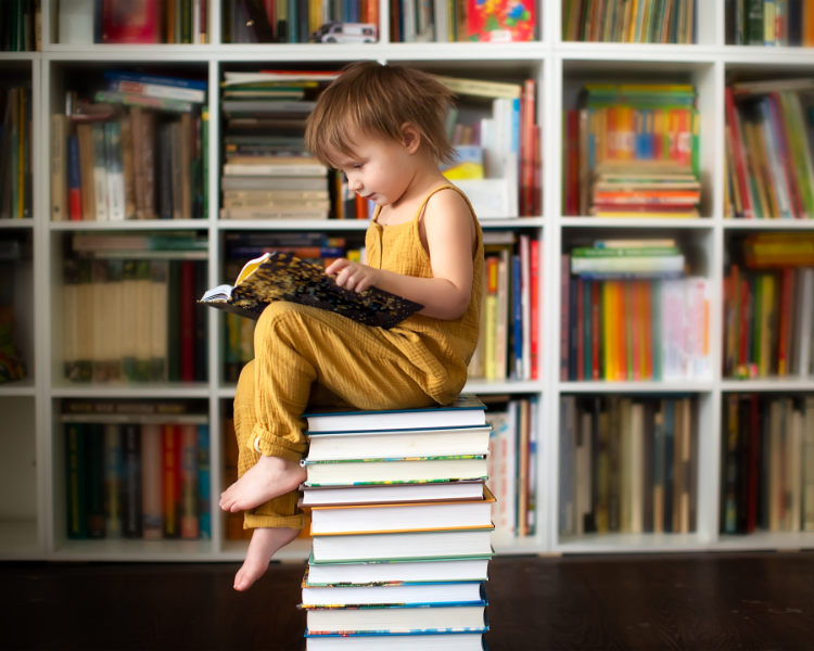 Child sitting on top of a large stack of books
